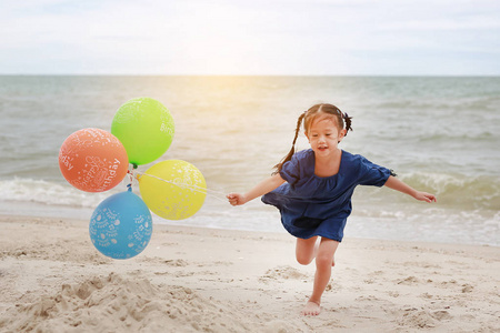 快乐的孩子与五颜六色的气球跑在海滩上