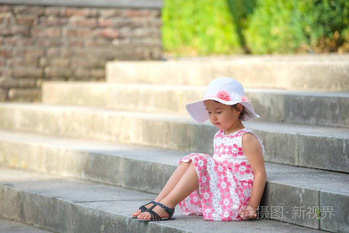 可爱的小女孩，戴着白帽，在温暖 阳光明媚的夏日坐在楼梯上