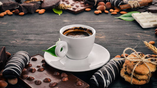 一杯咖啡和一组巧克力饼干和糖果。在黑色的木质背景。顶部视图。复制文本空间