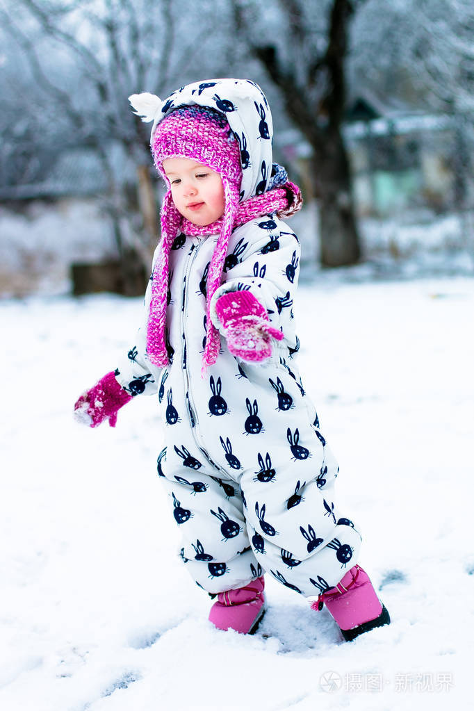 女婴在白色 snowsuite 和粉色的帽子,靴子手套在雪冬季公园照片-正版