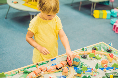 孩子们玩木制玩具, 在家里或托儿所建造玩具铁路。蹒跚学步的男孩玩起重机, 火车和汽车。学前和幼儿园儿童的教育玩具。软垫家具, 椅