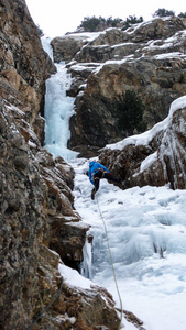男子冰登山者在蓝色夹克上的 gorgrous 冰冻瀑布攀登在阿尔卑斯山在深冬