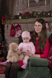 圣诞晚会。母亲和女儿坐在椅子上的壁炉和圣诞树