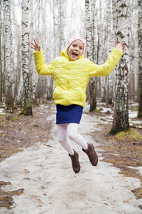 穿着黄色夹克的女孩在春天的森林里跳跃着乐趣