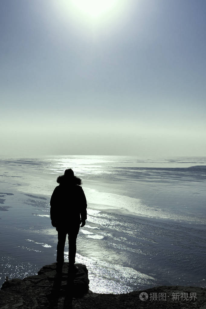 一个人的剪影留在高高的悬崖边缘冬天看太阳孤独的旅行者概念