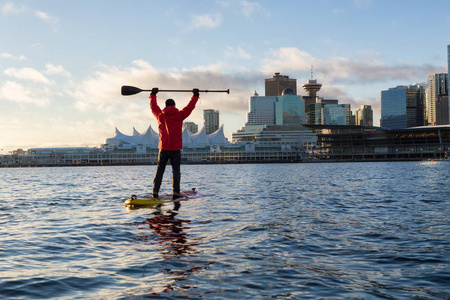 在一个充满活力的冬季日出期间, 有冒险精神的人正在市区附近划船。在加拿大不列颠哥伦比亚省温哥华的煤港拍摄