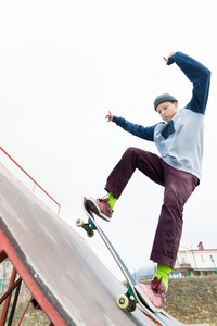 青少年选手在连帽运动衫和牛仔裤幻灯片的栏杆上踩着滑板在滑板公园