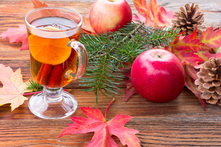 茶的肉桂和柠檬，熟透了的苹果，红色秋天枫叶，冷杉分支和松树球果在木桌特写