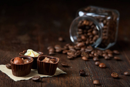 侧面视图翻转玻璃罐与咖啡豆和巧克力糖果在木质背景, 选择性焦点