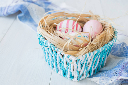 白色的仿古木制背景与巢上复活节彩蛋和蓝色篮子亚麻布上的毛巾选择性焦点