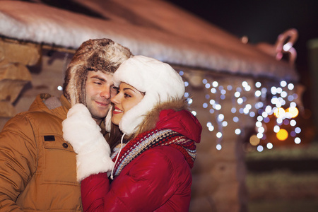 幸福的夫妇，在户外在晚上圣诞灯的爱