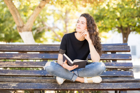 坐在公园长椅上的年轻女子一本书, 看着远离