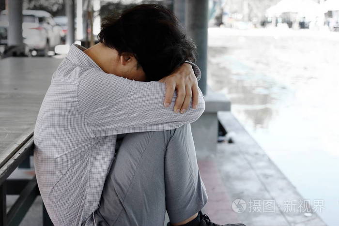 沮丧疲惫的年轻亚洲商人的侧面看着坐着抱着他的膝盖到胸部