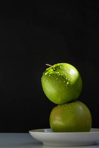 两个多汁的绿色苹果清洁是在桌子上的一个白色的飞碟。低键