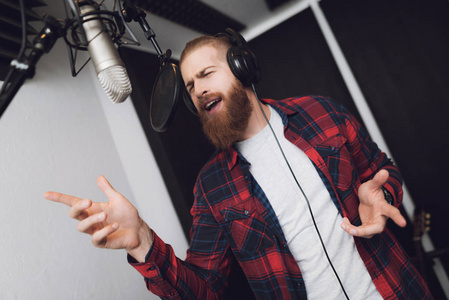 一个有胡子的男人在录音棚里表演一首歌.他穿着格子衬衫.