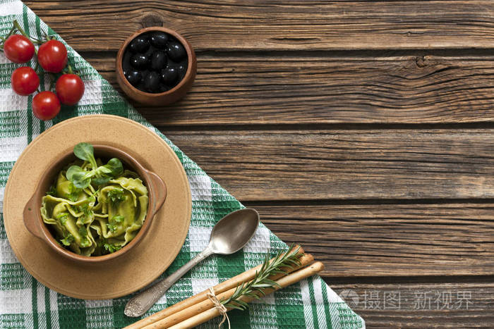 绿色意大利馄饨的特写视图与大教堂叶子, 橄榄和红色樱桃西红柿在木桌上