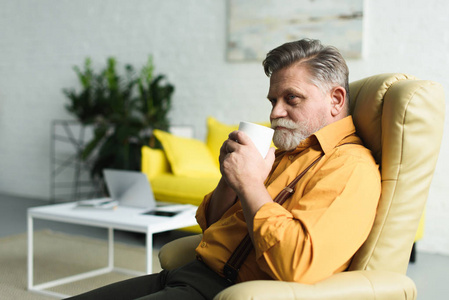 坐在扶手椅上的微笑胡子老人喝咖啡从杯子