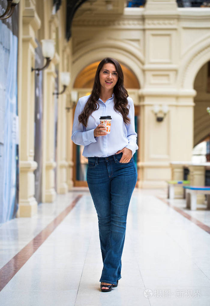 穿着蓝色牛仔裤和衬衫走路的年轻漂亮的黑发女人