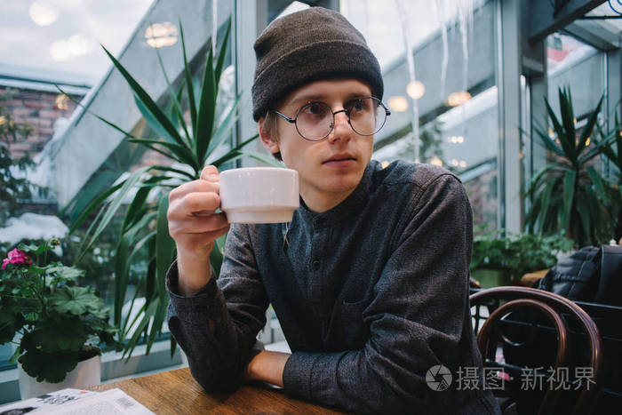 眼镜男在空闲的时间在一家咖啡馆里喝咖啡的年轻学生