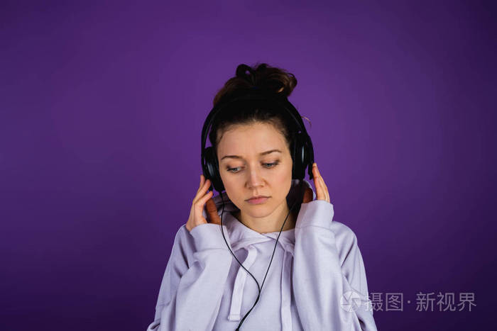 严肃的女孩听悲伤的音乐在耳机中的紫色背景运动衫