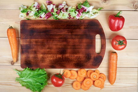 在木制背景下切板周围的新鲜蔬菜框架。健康的天然食物在桌上与拷贝空间在切削板。烹饪配料顶部视图, 食谱或菜单样机