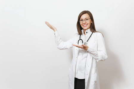 年轻的医生带着听诊器, 眼镜在白色背景下被隔离。女医生在医疗礼服指着手放在复制空间。医护人员, 健康, 医学概念