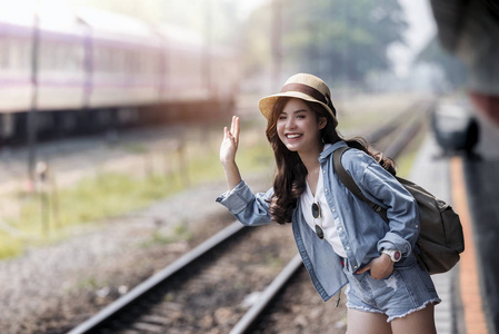 亚洲背包旅行女子在火车站站台暑期旅游或年轻旅游概念上微笑挥舞手