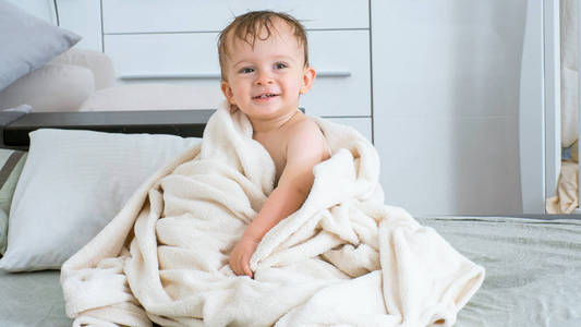 沐浴后欢快的幼儿男孩覆盖在白色毛巾的肖像