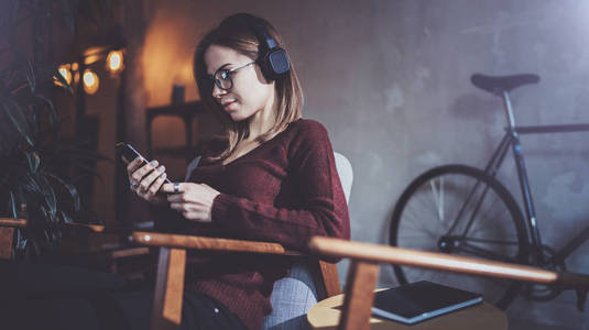 年轻迷人的时髦女孩戴眼镜和休闲服装听音乐在智能手机在现代的地方