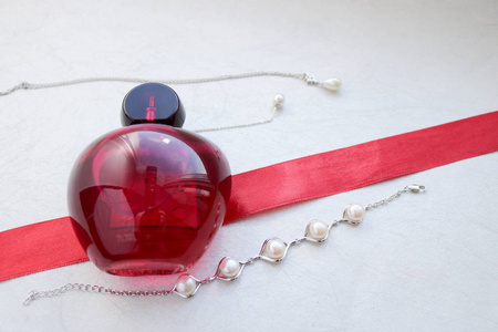 红色美丽的玻璃透明时尚迷人的一瓶女性香水躺在红丝带与单调的白色珍珠和地方为一个简单的文本在浅白色背景