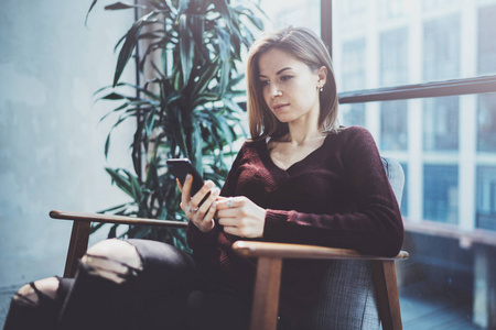 手持现代手机的金发青年女人。女孩指着手指在阳光明媚的 coworking 地方的空触摸移动屏幕。横向模糊背景