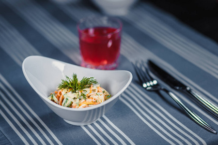 餐桌在餐厅。桌子上有一份白色盘子一把小刀一把叉子一杯红果汁的沙拉。桌子上有条蓝色桌布。