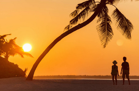 日落时两个孩子在热带海滩的剪影