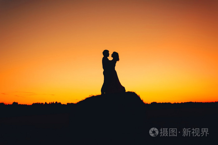对夫妇抱着橘黄色的夕阳为背景