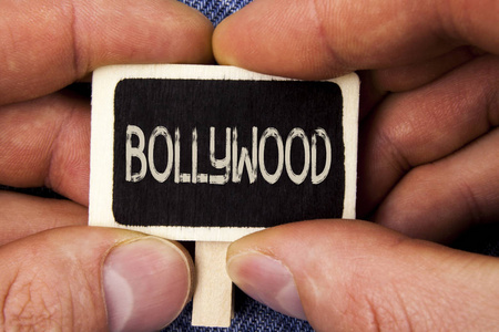 写的纸条显示宝莱坞。商业照片展示印度电影在蓝色牛仔裤背景上的人持有的木片上写的娱乐源