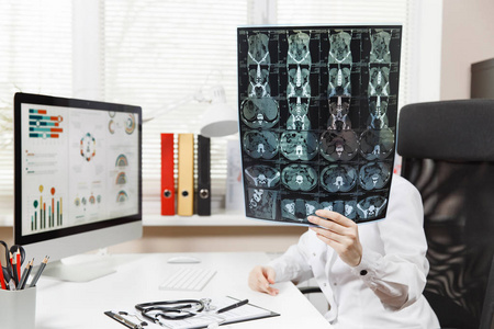 女医生坐在办公桌旁用电脑, 胶片 x 光脑部通过影像影像 ct 扫描 mri 在医院的轻型办公室。妇女在咨询室的医疗礼服。医疗保