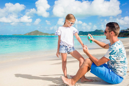 年轻的父亲在海滩上给女儿涂了防晒霜。防晒