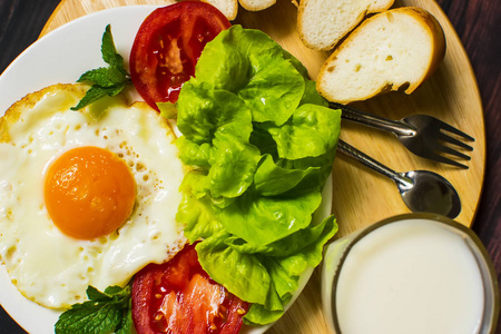早餐与面包, 煎蛋, 牛奶和蔬菜和油炸蕃茄片断在木头背景