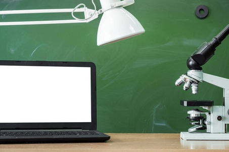 老师或学生桌。教育背景。教育理念。笔记本电脑用空白屏幕, 显微镜上的桌子上有台灯的黑板背景。化学或生物课