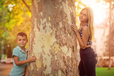 兄弟姐妹。男孩和十几岁的女孩摆在树干附近