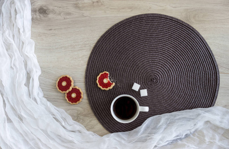 在一张白色和深色圆餐巾的木桌上躺着饼干, 红果冻向日葵种子是一杯咖啡屑