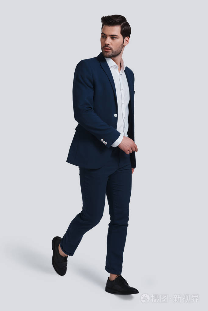 全长的英俊的年轻人在完全西装步行反对灰色背景