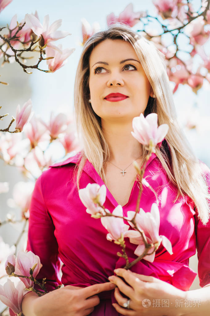 穿着粉红色连衣裙的漂亮金发女郎的户外画像, 在春天盛开的花朵上摆