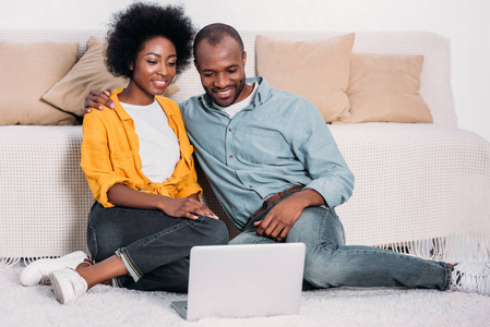 微笑的非洲裔美国人夫妇在家看电影在膝上型电脑