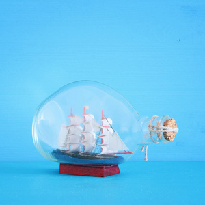 航海概念图片与风帆小船在瓶在蓝色木桌和背景。选择性聚焦