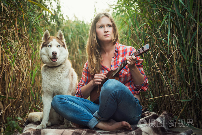 年轻的白种女人玩的四弦琴。女性与哈士奇狗玩吉他在户外