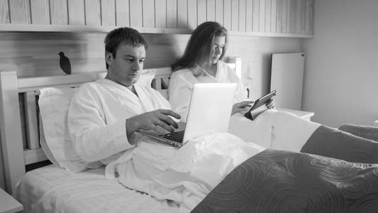 年轻夫妇的黑色和白色的形象在床上工作, 在早上的商人和商人