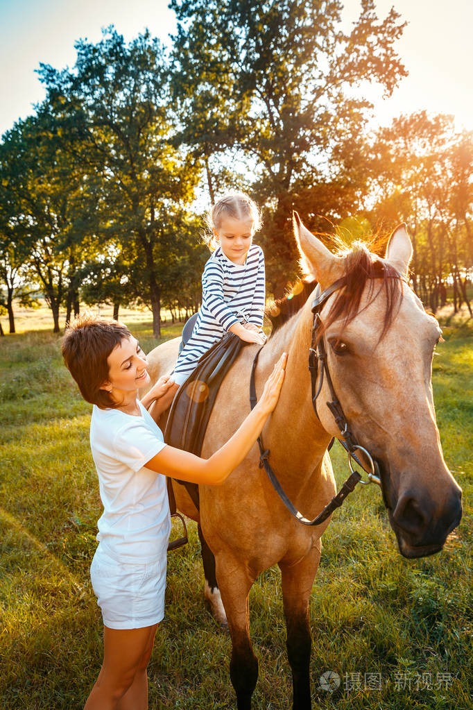 骑在马背上与她的母亲站在旁边的小女孩