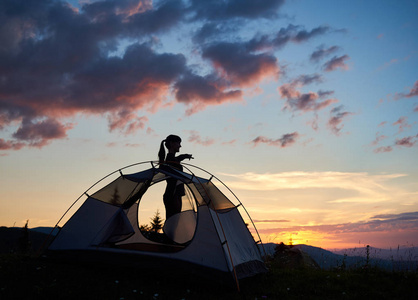 小女孩站在帐篷附近的轮廓, 显示她的手在清晨的天空下的黎明与令人难以置信的山脉和上升的太阳在他们上面的距离。通过帐篷查看