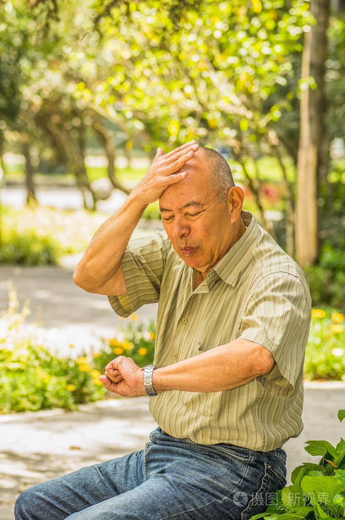 老人的户外观坐在板凳上匆忙, 因为没有足够的时间看他的手表在公园